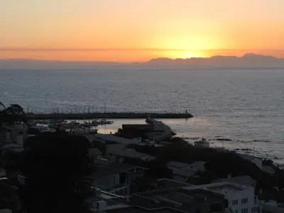 a sunset over the ocean with houses and a harbor at View Panoramica Self-Catering Apartment in Gordonʼs Bay