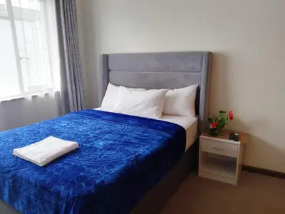 a bed in a room with a blue blanket and a window at Twinex Accommodation Bellville in Stikland