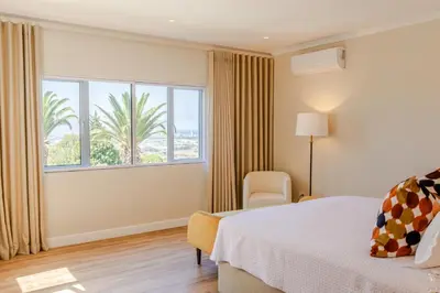 a bedroom with a bed and a chair and a window at The Helderview Luxury Suites in Somerset West