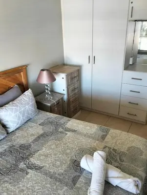 a bedroom with a bed and a dresser and a lamp at Hermanus Beach Club 223 in Hermanus