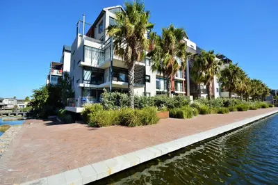 a building next to a river with palm trees at Quayside 1 Bedroom Apartment in Century City in Cape Town