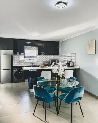 a kitchen with a glass table and blue chairs at Goodness Century Apartment in Cape Town