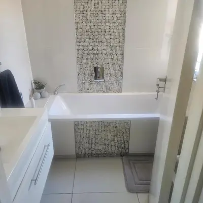 a white bathroom with a tub and a tile wall at Mimi's in Plattekloof