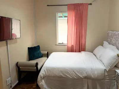 a bedroom with a bed and a chair and a window at Miches House in Cape Town