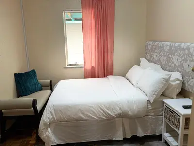 a bedroom with a bed and a chair and a window at Miches House in Cape Town