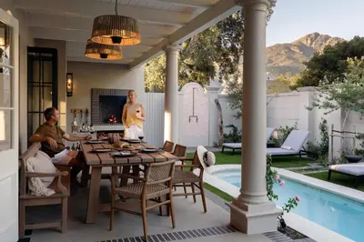 a family sitting around a table on a patio with a pool at Pink Door Franschhoek by The Oyster Collection in Franschhoek