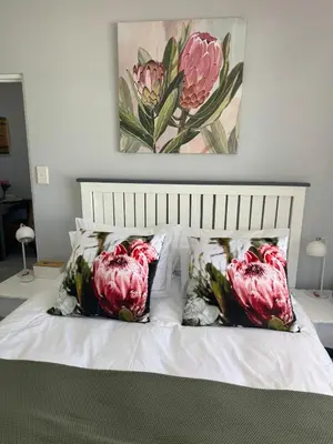 a bed with three pillows and a painting on the wall at The Protea & Vine - Paarl - Self Catering Apartment in Paarl