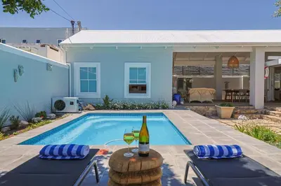 a swimming pool with a bottle and two glasses of wine at Nautilus on Grotto Beach - heated pool in Hermanus