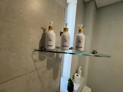 a group of four bottles on a glass shelf in a bathroom at Black & White Self Catering in Paarl