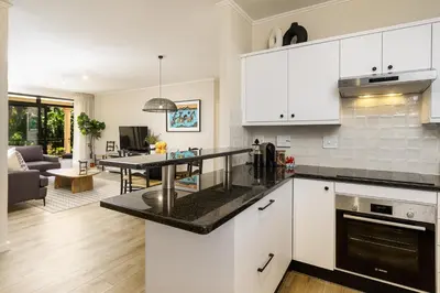 a kitchen with white cabinets and a living room at Canal Front Apartment Cape Town in Cape Town