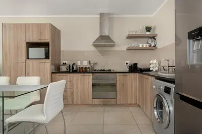 a kitchen with wooden cabinets and a table and white chairs at Mayfair 134 in Cape Town