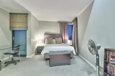 a bedroom with a bed and a desk and a fan at Luxury Mini Villa Sunset Beach Cape Town in Cape Town