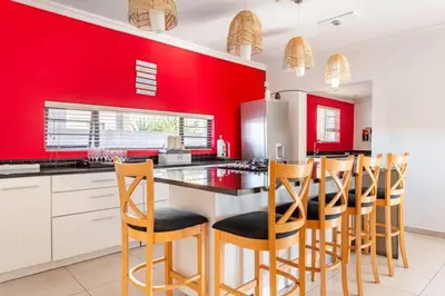 a kitchen with red walls and wooden bar stools at Cheap Affordable Self-Catering Double Room with Pool, WiFi and Braai in Cape Town