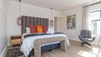 a bedroom with a large bed and a chair at Ocean Whisper Villa near Westcliff coastal paths in Hermanus