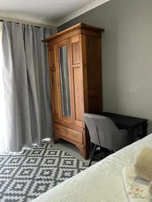 a bedroom with a wooden cabinet and a desk and a bed at Three on Firmount in Somerset West