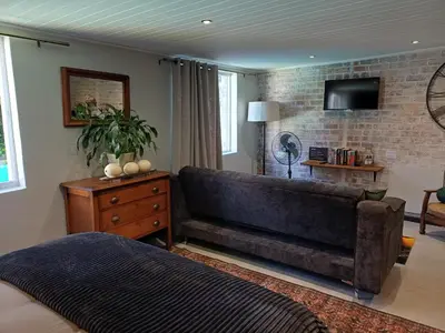 a bedroom with a large couch and a tv on a brick wall at 7th Heaven Guest Cottage in Paarl