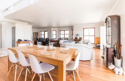 a dining room with a wooden table and white chairs at Geheim Luxury Seafront in Hermanus