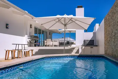 a swimming pool with an umbrella next to a house at Mimosa Voelklip Retreat in Hermanus