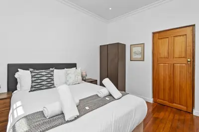 a bedroom with a white bed with a wooden door at Spacious Claremont Home with Pool Fireplace in Cape Town