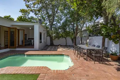 a swimming pool in a backyard with a table and chairs at Spacious Claremont Home with Pool Fireplace in Cape Town