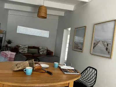 a wooden table in a living room with a table and chairs at BEACHees - cute central cottage in Kleinmond
