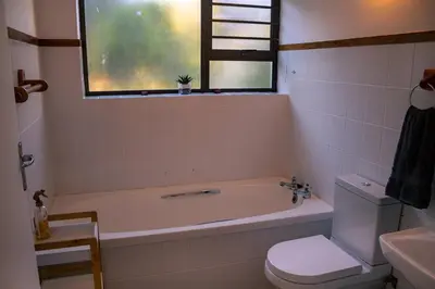 a bathroom with a tub and a toilet and a window at Voëlklip Family House in Hermanus