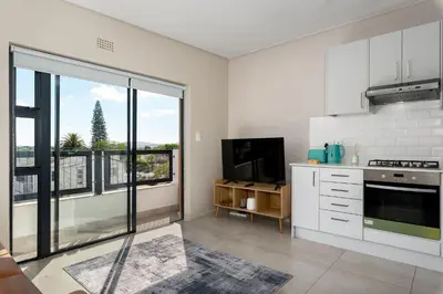 a kitchen with white cabinets and a large window at Breeze of the Sea Apartment in Cape Town