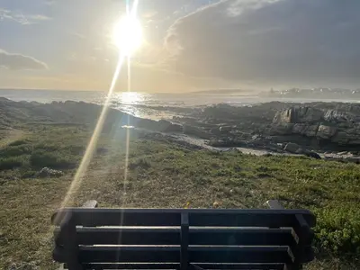 a bench sitting on top of a hill with the sun at Barking Beach Cottage, Sandbaai - Pet Friendly in Hermanus