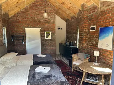a bedroom with two beds and a brick wall at Garden Studio in Greyton
