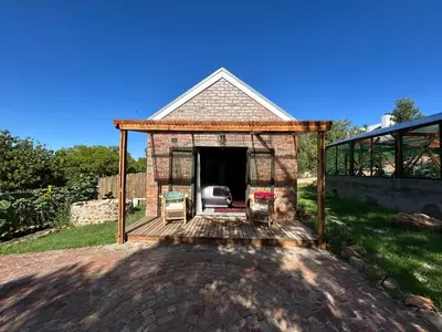 a brick house with a deck with two chairs at Garden Studio in Greyton