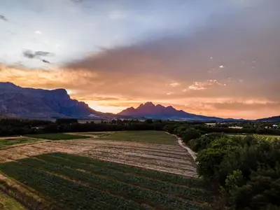 a sunset over a field with mountains in the background at Franschhoek Homestead Cottage in Groendal