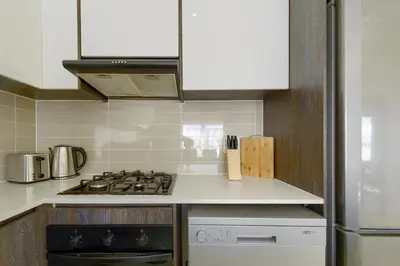 a kitchen with a stove top oven and white cabinets at Chic & Cozy Apartment with Pool, Gym & Balcony - The Sandown in Cape Town