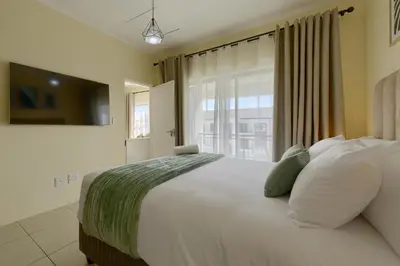 a bedroom with a large white bed with a window at Chic & Cozy Apartment with Pool, Gym & Balcony - The Sandown in Cape Town