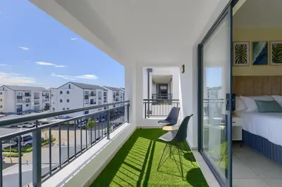 a bedroom with a bed and a balcony at Chic & Cozy Apartment with Pool, Gym & Balcony - The Sandown in Cape Town
