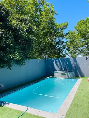 a blue swimming pool with a fence and trees at ANNIKA B&B Claremont in Cape Town