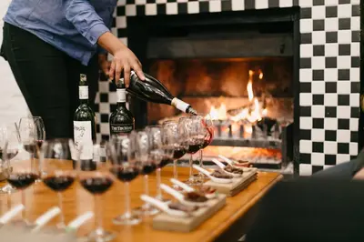 a person pouring wine into wine glasses in front of a fireplace at Zevenwacht Cottages in Kuilsrivier