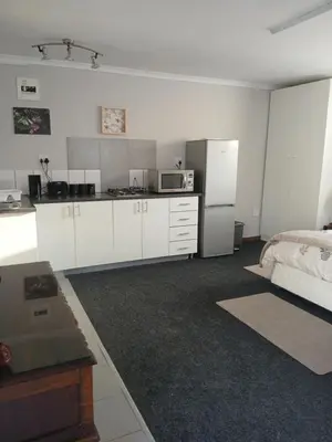 a kitchen with white cabinets and a bed in a room at Cozy, self-catering Garden Flat in Cape Town