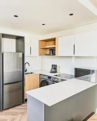 a kitchen with white cabinets and a stainless steel refrigerator at Bethany Apartment ON PARK Century City in Cape Town