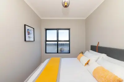 a bedroom with a bed with white and yellow pillows at Cape on Porterfield in Cape Town