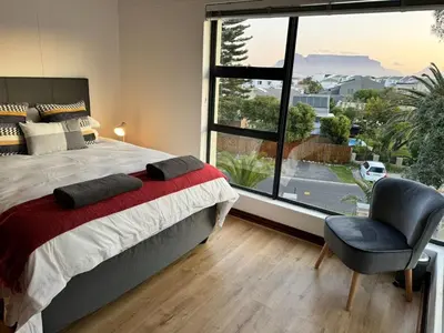 a bedroom with a bed and a chair and a large window at Peaceful 2-Bed Apartment in Boubergstrand in Cape Town