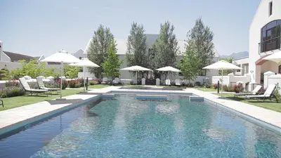 a swimming pool with chairs and umbrellas next to a building at Winelands Golf Lodges 30 in Stellenbosch