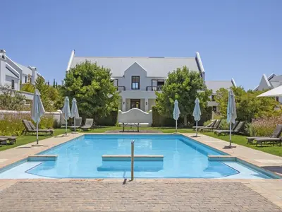 a pool with chairs and umbrellas in front of a house at Winelands Golf Lodges 33 in Stellenbosch