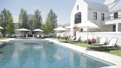 a swimming pool with chairs and umbrellas next to a house at Winelands Golf Lodges 33 in Stellenbosch