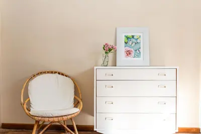 a white chair next to a dresser with a vase of flowers at The Kleinmond Cottage in Kleinmond