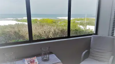 a room with two windows and a white chair and a table at Strandloper Apartments in Hermanus