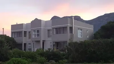 a white building with a mountain in the background at Strandloper Apartments in Hermanus