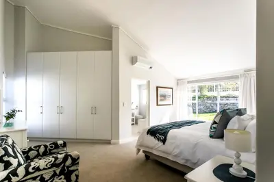 a white bedroom with a bed and a chair at The Joyful Tortoise in Hermanus