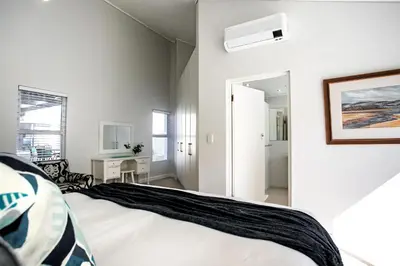 a white bedroom with a bed and a bathroom at The Joyful Tortoise in Hermanus