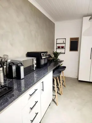 a kitchen with a counter with a microwave and some chairs at Apartment in Gordon's Bay in Gordonʼs Bay