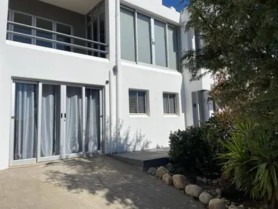 a white house with large windows and a driveway at Apartment in Gordon's Bay in Gordonʼs Bay